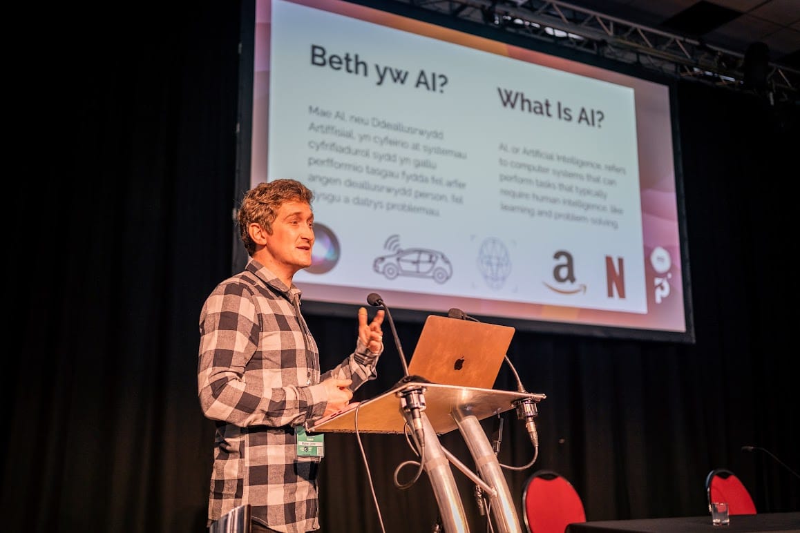 Andrew, a trainer on the course talking on a stage in front of a slide saying 'What is AI'