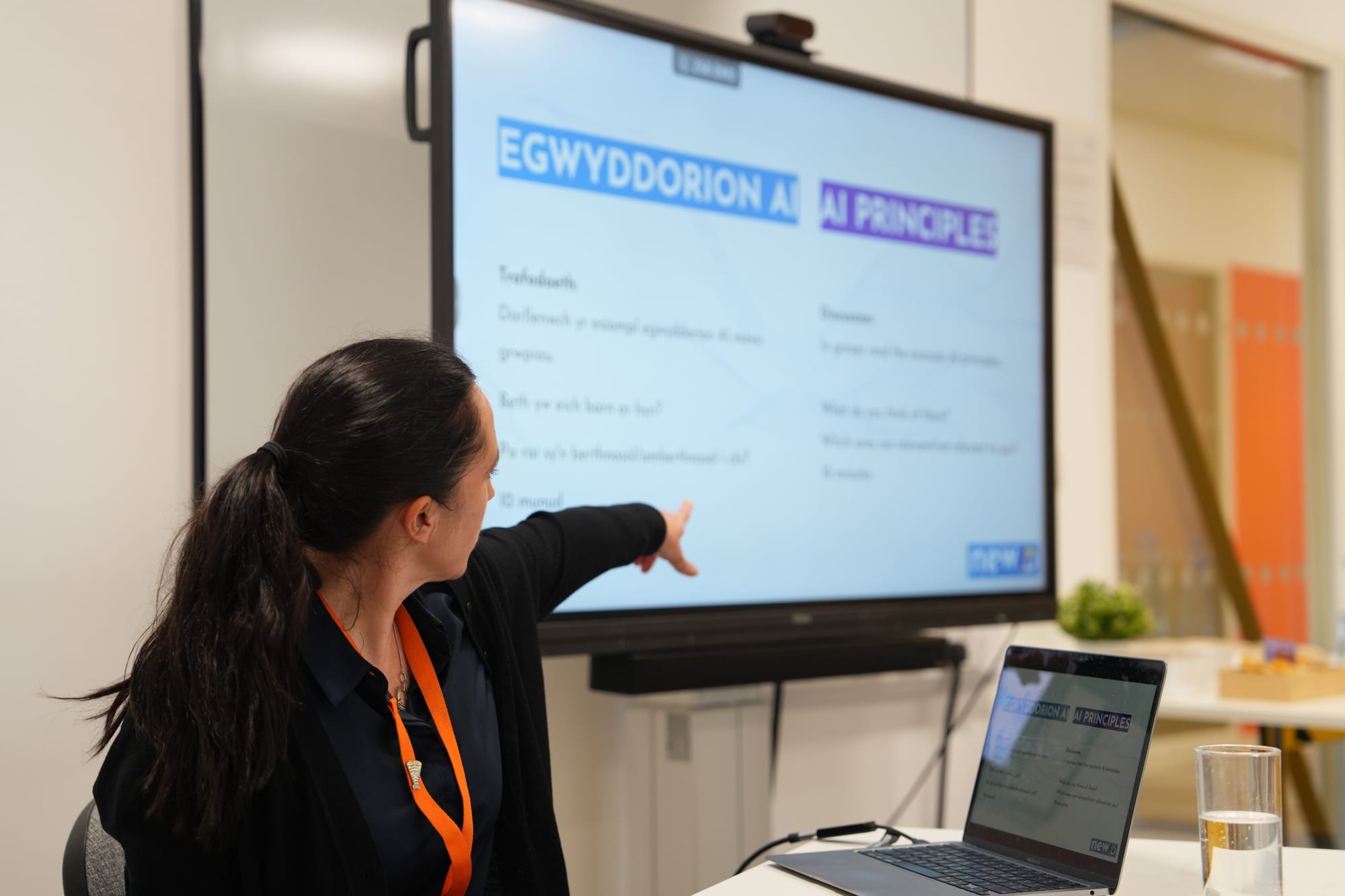 Trainer pointing to a bilingual slide that says Principles of AI in Welsh and English
